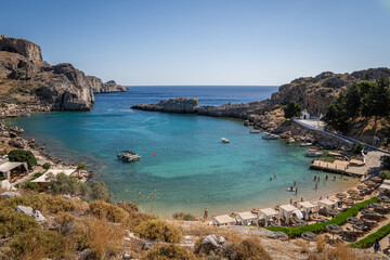 Fototapeta na wymiar Picturesque Bay in Lindos, Rhodes: A serene sanctuary where a beautiful beach, moored boats, and the captivating turquoise embrace of the Mediterranean converge.