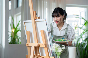 Young female artist works on abstract acrylic painting on canvas in art painting studio.