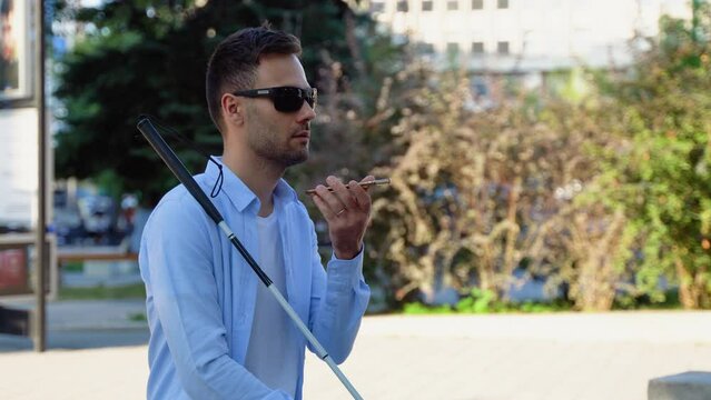 Blind man wearing sunglasses sitting on bench holding cane and talking into phone