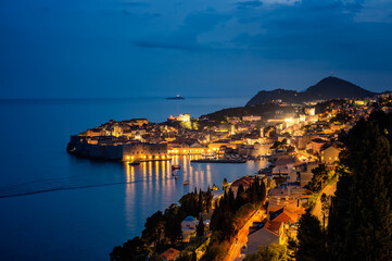 Amazing aerial panoramic view of the picturesque town of Dubrovnik with the old town, illuminated streets and buildings and marina with boats at night.