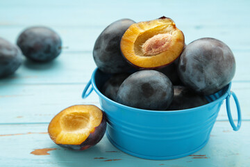 Fresh plums on metal bowl on blue wooden background