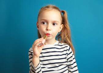 Happy little girl puts lipstick on her lips on blue background. Little trendy. little girl applying makeup