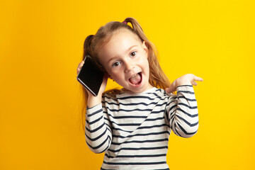 Funny little girl talking on mobile phone on yellow background.