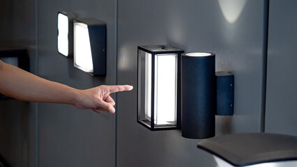 Designer hand pointing at sample of exterior LED wall lamp in home design store. Modern box shape...