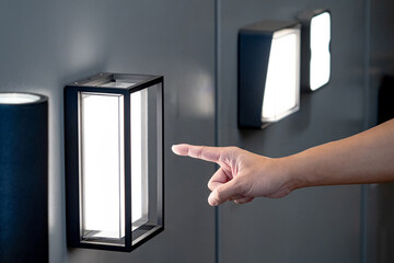 Designer hand pointing at sample of exterior LED wall lamp in home design store. Modern box shape light fixture mounted on wall for outdoor lighting