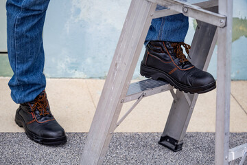 Male maintenance worker feet with protective safety shoes climbing up on aluminum step ladder at...