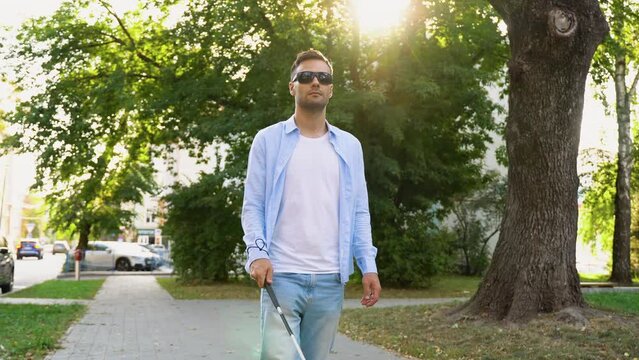 Young blind man walks with a cane on a street