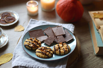 Cup of tea or coffee, plate with desserts, dried oranges, bowl of grapes, scented candles, vintage books, pumpkins and autumn leaves on the table. Autumnal hygge. Selective focus.