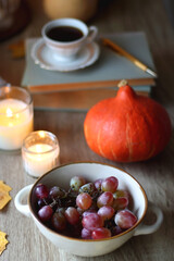Obraz na płótnie Canvas Cup of tea or coffee, plate with desserts, dried oranges, bowl of grapes, scented candles, vintage books, pumpkins and autumn leaves on the table. Autumnal hygge. Selective focus.