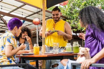 A group of friends from the lgbt community gathered at a restaurant enjoying a delicious meal and taking cell phone pictures of the food. - obrazy, fototapety, plakaty