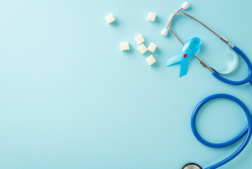 Mark Diabetes Awareness Month with top-view diabetes emblem - blue ribbon with blood drop. Complementing image are stethoscope and granulated sugar on soft blue backdrop, space for text or promotion