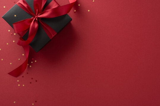 Luxury gifting: A top-view shot of a sophisticated black gift box adorned with a red ribbon, set amidst golden star-shaped confetti on a marsala background, with room for your custom text