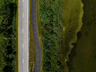 Top down view over an empty road, next to an empty bicycle path surrounded by lush green