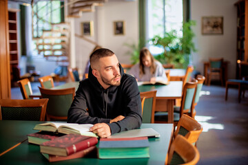 Young male student sitting in the university library and learning