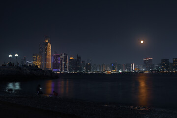 Abu dhabi city skyline at night and rise of full moon