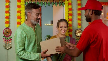 Senior couples receiving parcel or package from delivery person at home door during Diwali festival day - concept of online order, quick commerce and festive gift or present