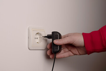 Man hand inserts an electrical plug into outlet closeup