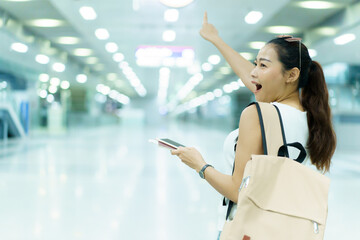 Happy beautiful Asian solo female tourist walking in the airport terminal, woman walking and talking with her friend on mobile phone. Asian woman passenger walks in airport terminal to departure gate.