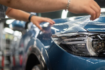 The master in the car service applies a protective armor film to the car body.  - obrazy, fototapety, plakaty