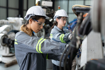 Female engineer checking and maintaining robot arms machine at factory. Technician woman in uniform with helmet safety repairing robotic arms for automated manufacturing industry
