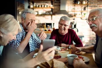Group of senior friends using a smartphone while having breakfast together in the kitchen