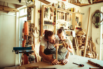 Young carpenter father teaching his daughter how to assemble wood in the garage - obrazy, fototapety, plakaty