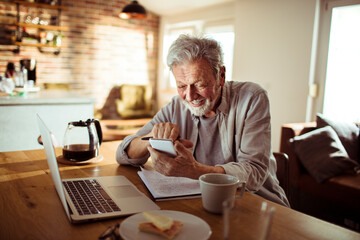 Senior man using a smartphone at home - obrazy, fototapety, plakaty