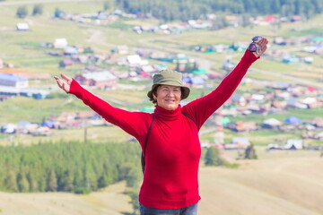 a beautiful mature woman stands on the top of Mount Kraka and looks into the distance at the Ural village of Shigaevo in the southern Urals on a summer sunny day