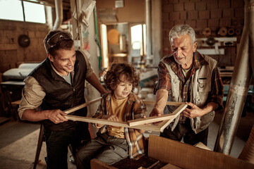 Multigenerational family of male carpenters teaching their youngest one the ways in a carpentry shop