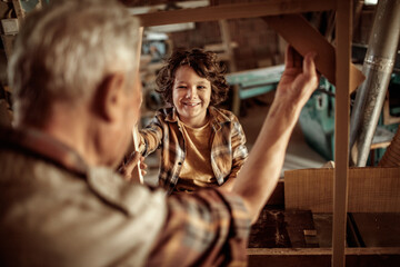 Obraz na płótnie Canvas Senior male carpenter showing his grandson a wood frame in a carpentry shop