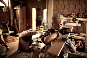 Senior male carpenter measuring wood in a carpentry shop - obrazy, fototapety, plakaty