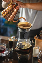 drip coffee, Barista making drip coffee by pouring spills hot water on coffee ground with prepare filter from copper pot to glass transparent chrome drip maker on wooden table in cafe shop