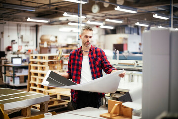 Middle aged Caucasian man carrying a sheet of paper in a printing press office