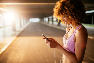 Young fit woman using a smartphone before jogging under a bridge in the city