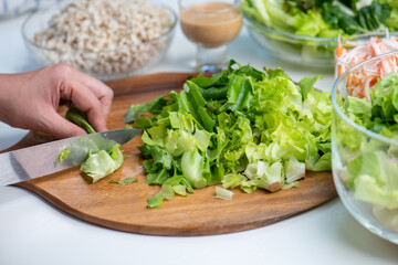 Hand cut and slice fresh baby cos salad on wood board table .Organic Vegetables mix lunch with green vegetables at kitchen table on wood cutting board.
