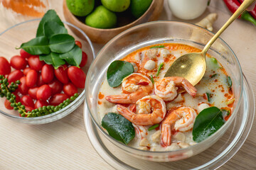 Tom Yam Kung or Tom Yum soup is Thai hot spicy soup shrimp or prawn with lemon grass, lemon, galangal, mushrooms, coconut milk and chili in bowl on wooden table top view, famous Thai food cuisine.