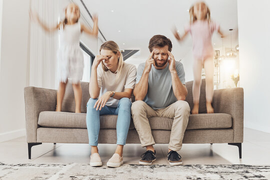 Frustrated parents, sofa and headache with children jumping in living room chaos, ADHD or crazy home. Mother and father in stress, burnout or fatigue with busy or hyper active kids in lounge at house