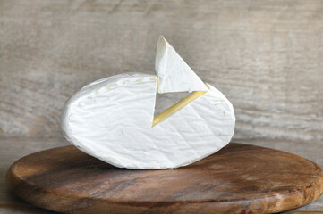 Soft brie cheese close-up with a cut out triangle on a wooden background. Front view, daylight