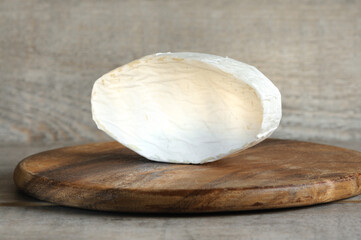 Soft brie cheese close-up. Oval shaped cream cheese whole piece on a wooden board and on a gray wooden background. Beautiful daylight with shadows