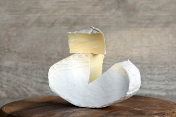 Soft brie cheese close-up with a cut out segment on a wooden background. Front view, daylight, rays and shadows