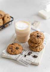 Stack of delicious freshly baked oatmeal cookies with nuts and chocolate drops and a glass of latte...