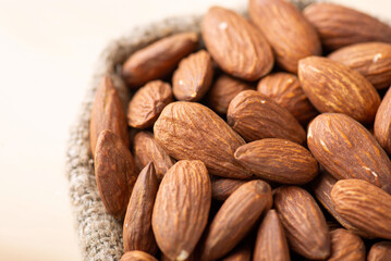 Top view of almonds in small bag. Close up shot of fresh tasty almond nuts in bag made of linen fiber on light background