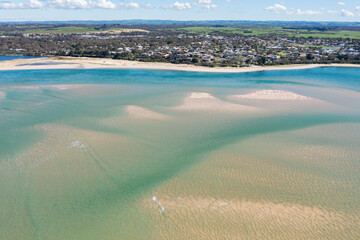 Aerial view of sand bars and patterns in a shallow inlet alongside a coastal town