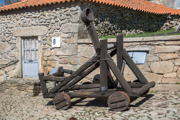 View of a medieval wooden catapult, a decorative piece in the 25 Abril square, and iconic Penedono Castle, on Penedono village downtown, Viseu, Portugal - obrazy, fototapety, plakaty