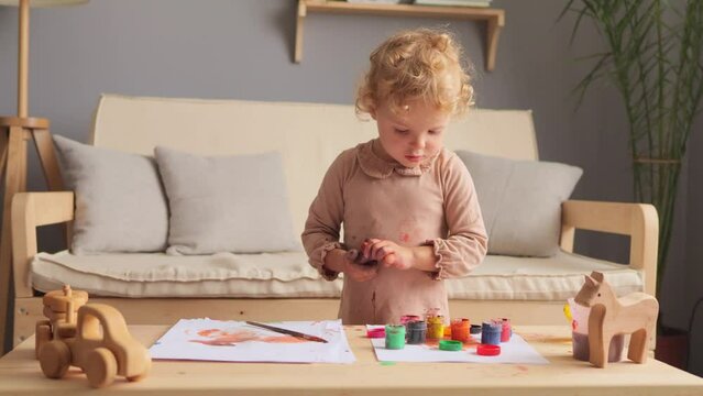 Funny childhood art. Toddler painting fun. Creative little artist. Adorable baby drawing. Charming wavy haired toddler child drawing at home using colorful paints at home or nursery.