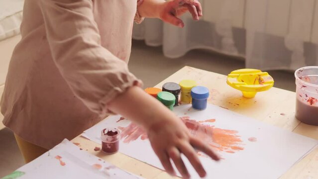 Concentrated baby girl learning painting with water colors in light room interior finishing her artwork closed bottle with paint creative exploration enjoying time of discovery and colorful expression