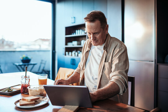 Middle aged man using the tablet while having breakfast in the kitchen