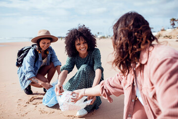 Trio of diverse friends recycling plastic waste from a beach