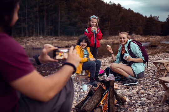 Young father taking a picture on a smartphone of his family while out camping in the forest together