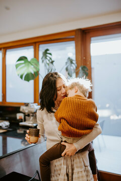 Mother holding and comforting her young son in the kitchen at home
